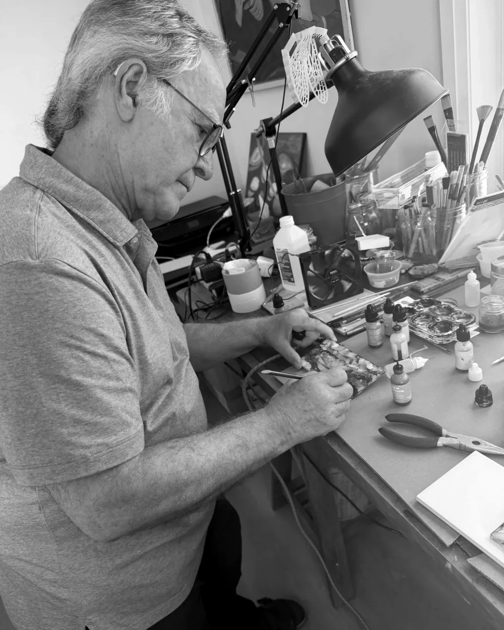 Manfred at his studio table, working on a small alcohol ink painting surrounded by ink bottles and brushes